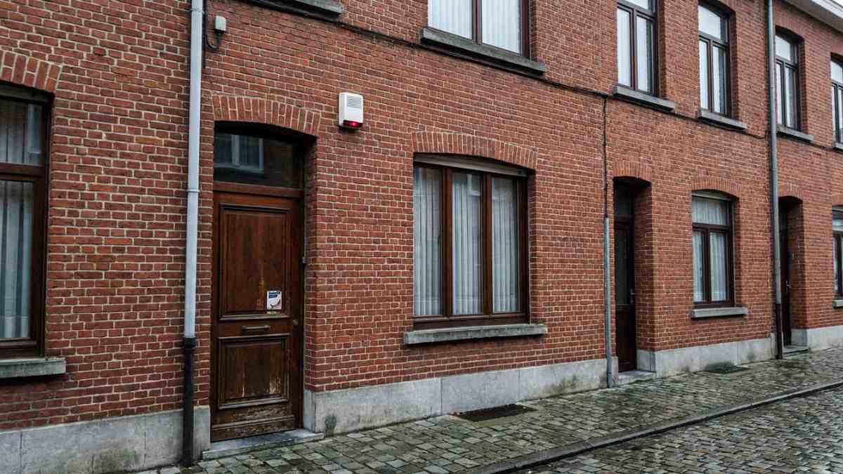 La façade d'une maison belge avec un boîtier de sirène d'alarme et un autocollant de sécurité sur la porte d'entrée. 